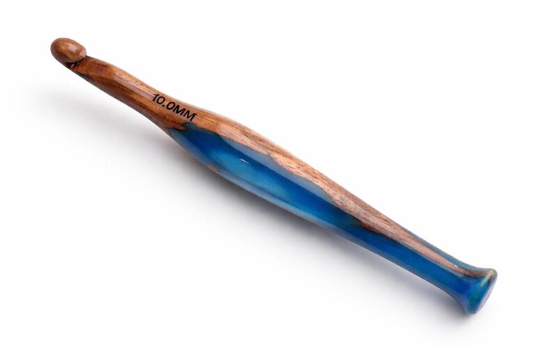 Pu&ograve; includere: Un uncinetto con manico in legno venato marrone combinato con una sezione in resina blu traslucida. L'uncinetto presenta una punta affusolata e un'estremit&agrave; svasata, con il testo 10.0MM chiaramente stampato in nero sulla parte in legno.