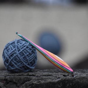 May include: A ball of dark blue yarn and a colorful wooden crochet hook on a gray textured surface.