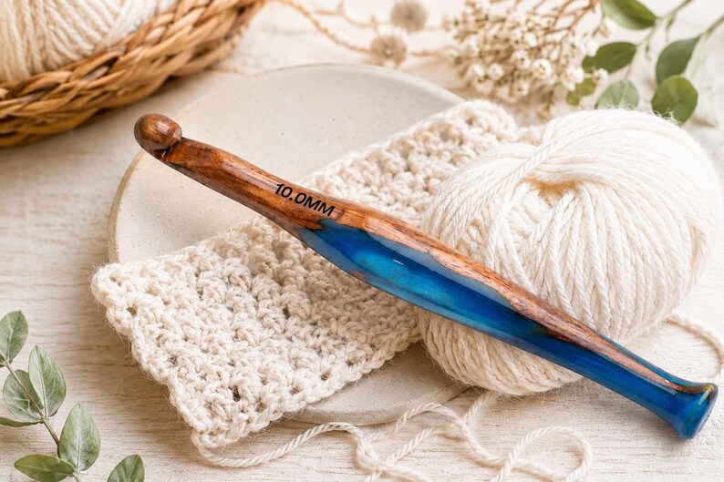 Pu&ograve; includere: Un uncinetto da 10,0 mm con un manico realizzato in una combinazione di legno marrone naturale e resina blu traslucida. L'uncinetto presenta un collo liscio e affusolato e una testa arrotondata, con la misura 10,0 mm stampata in nero sul legno.
