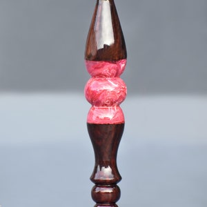 May include: A wooden spinning wheel spindle with a pink and white marbled design in the center.