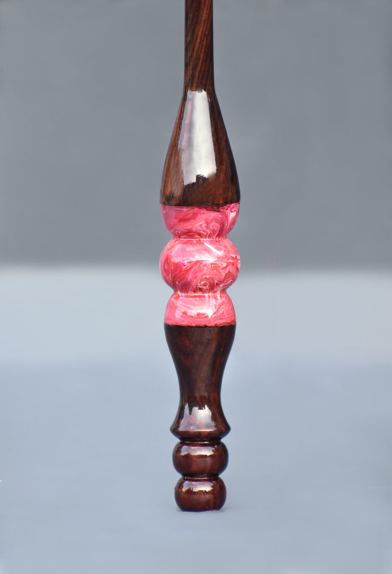 May include: A wooden spinning wheel spindle with a pink and white marbled design in the center.
