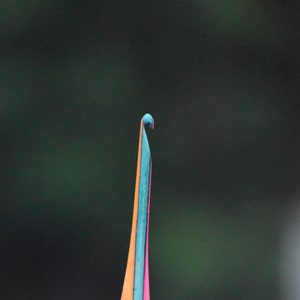 May include: Close-up of a colorful, thin, pointed object with a curved tip. The object is a vibrant mix of orange, blue, and pink.