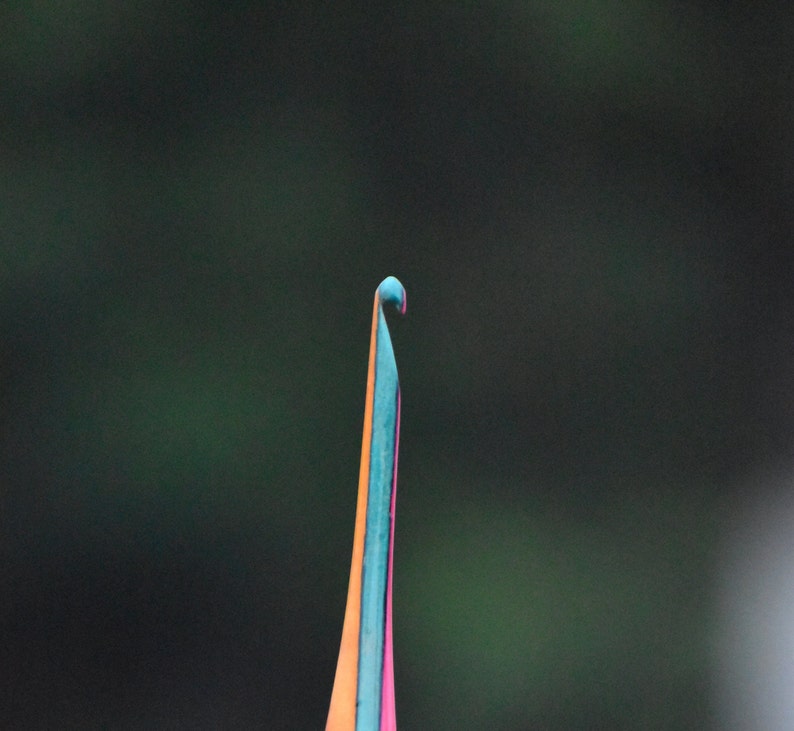 May include: Close-up of a colorful, thin, pointed object with a curved tip. The object is a vibrant mix of orange, blue, and pink.