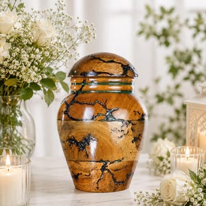 May include: A wooden cremation urn with a polished finish, featuring a rounded lid and a bulbous body. The natural wood grain is accented by dark, branching crack patterns filled with a vibrant teal resin inlay that wraps around the vessel.
