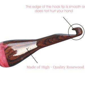 May include: A close-up of a wooden crochet hook with a pink and brown resin handle. The hook tip is smooth and rounded. "Made of High - Quality Rosewood and Resin" is written below the hook.