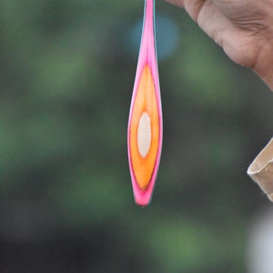 May include: A long, thin, wooden object with a pink, orange, and white design. The object is cut in half lengthwise, revealing the wood's natural grain.