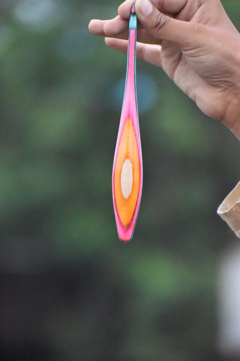 May include: A long, thin, wooden object with a pink, orange, and white design. The object is cut in half lengthwise, revealing the wood's natural grain.