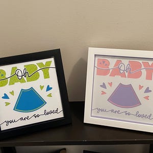 May include: Two framed prints with the text "Oh Baby" in green and pink letters. The prints feature a blue and purple ultrasound image with hearts and the text "You are so loved".
