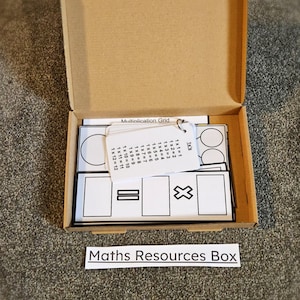 May include: A cardboard box with a white label that says "Maths Resources Box". The box contains a set of multiplication flashcards and a multiplication grid.