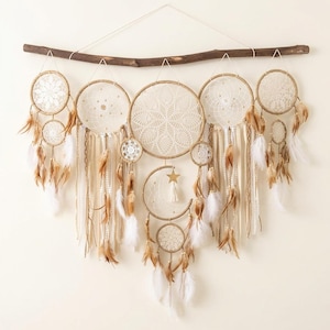 May include: A large wall hanging featuring five circular dream catchers and a crescent moon shape suspended from a dark wooden branch. The hoops are wrapped in tan cord and contain white lace webs, accented with hanging ribbons, feathers, and a star.