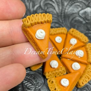 May include: Close-up of miniature pumpkin pie slices. Each slice features a golden-brown crust, a vibrant orange filling, and a dollop of white cream. The text "Dream Time Clays" is visible on the image.