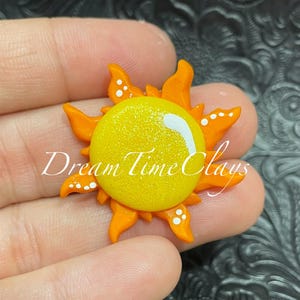 May include: A yellow sun with orange rays and white dots. The sun is made of polymer clay and has a glittery finish.