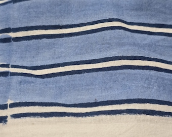 May include: A woven fabric featuring a pattern of horizontal stripes in shades of light blue, dark navy blue, and off-white. The textile displays a visible weave texture with consistent line spacing throughout the material, showcasing a repeating striped design.