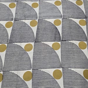 Puede incluir: Una tela blanca con un patrón geométrico repetitivo de semicírculos con rayas horizontales negras y círculos sólidos de color amarillo mostaza. El diseño está dispuesto en una cuadrícula sobre toda la superficie del material textil.