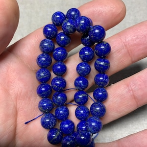 Op de afbeelding: Een streng diepblauwe lapis lazuli kralen met gouden vlekken. De kralen zijn rond en glad en zijn geregen op een dun draad.