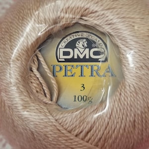 May include: A spool of DMC Petra size 3 crochet thread in a light tan color. The label reads "DMC PETRA 3 100%" with the DMC logo. The thread is wrapped in clear plastic.