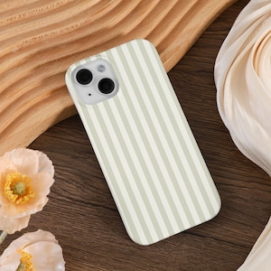 May include: A smartphone case with a vertical striped pattern in light green and white. The case has a camera cutout and is resting on a wooden surface. The overall aesthetic is minimalist and modern.
