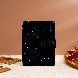 Puede incluir: Funda negra para lector electrónico con un patrón de constelación de estrellas blancas sobre un fondo negro.