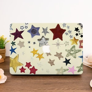May include: A laptop computer with a cream-colored case covered in a variety of colorful star-shaped stickers. The stars are in different sizes, shapes, and patterns, including a few with a swirl design.