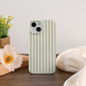 May include: A smartphone case with a vertical striped pattern in light green and white. The case is made of a hard material and has a camera cutout. The case is on a wooden surface with a flower and plant in the background.