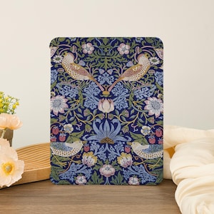 May include: A rectangular decorative item with a detailed floral and bird pattern. The design features birds, flowers, and berries in shades of blue, pink, and green on a dark blue background. The item is placed on a wooden surface.