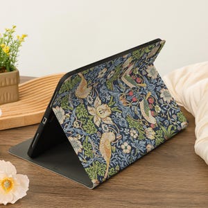 May include: A tablet case with a colorful floral and bird pattern in shades of blue, green, and cream. The case is open, revealing the tablet screen. The design features stylized birds, flowers, and foliage.
