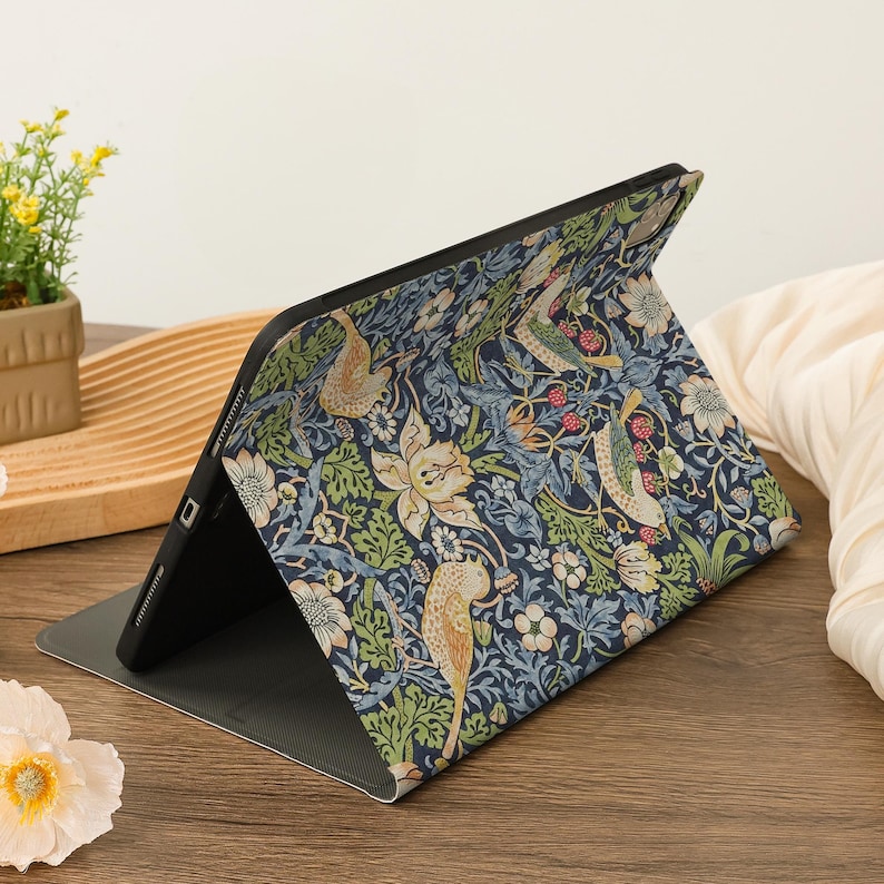 May include: A tablet case with a colorful floral and bird pattern in shades of blue, green, and cream. The case is open, revealing the tablet screen. The design features stylized birds, flowers, and foliage.