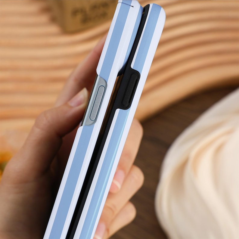 May include: A blue and white striped phone case with a black bumper. The case is closed and being held in a hand.
