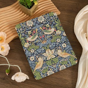 May include: A rectangular, patterned fabric with a dark blue background. The design features birds, flowers, and berries in shades of green, cream, and red. The fabric is likely used for a tablet or book cover.
