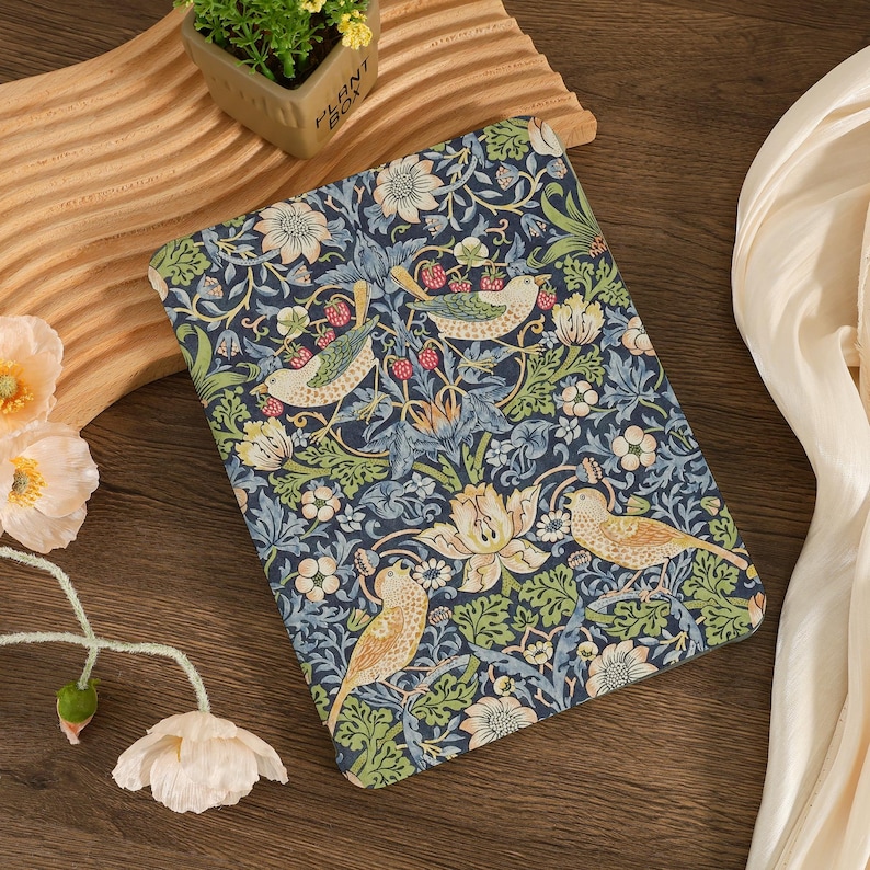 May include: A rectangular, patterned fabric with a dark blue background. The design features birds, flowers, and berries in shades of green, cream, and red. The fabric is likely used for a tablet or book cover.