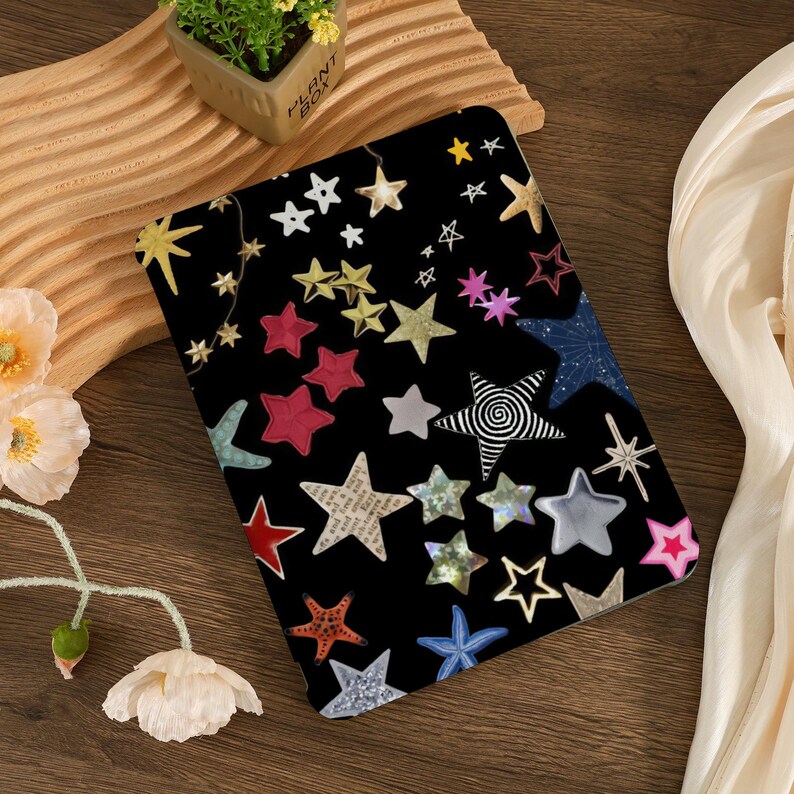 Pu&ograve; includere: Una custodia per iPad nera con un motivo a stelle colorate. Le stelle sono di vari colori, tra cui rosso, blu, verde, giallo e rosa. Alcune stelle hanno un design a spirale. La custodia ha uno sfondo nero.