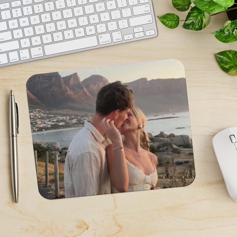 Peut inclure: Un couple s'embrassant devant une cha&icirc;ne de montagnes et l'oc&eacute;an. L'homme porte une chemise blanche et la femme porte une robe blanche.