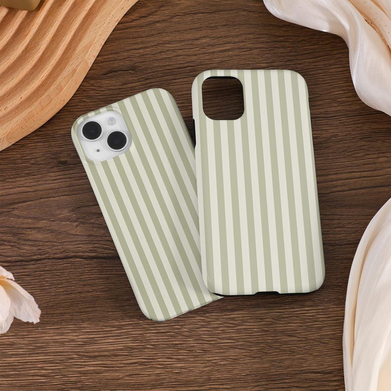May include: Two phone cases with a vertical striped pattern in light green and white. The cases are made of a smooth material and have cutouts for the camera and buttons. The cases are displayed on a wooden surface.