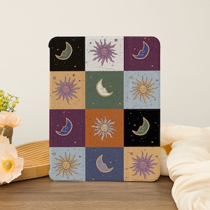 May include: A digital illustration of a repeating pattern of suns and moons with faces. The pattern is on a white background with a grid of different colored squares. The colors are purple, green, orange, blue, and black.
