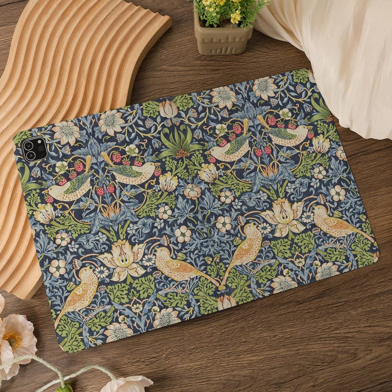May include: A tablet case featuring a detailed floral and bird pattern in shades of blue, green, and cream. The design includes stylized birds, flowers, and berries, creating a vintage aesthetic. The case is designed to fit a tablet.
