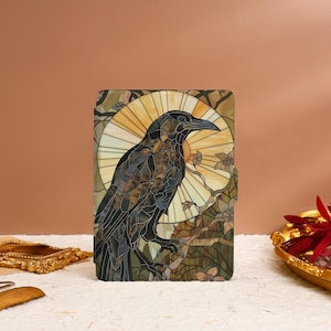 May include: A decorative case featuring a stained-glass style raven design. The raven is black and brown, set against a yellow sunburst background. The case has a rectangular shape and is decorated with floral accents.