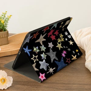 Pu&ograve; includere: Una custodia nera per iPad con un motivo a stelle colorate. Le stelle sono di varie forme e dimensioni e sono disposte in modo casuale. La custodia &egrave; realizzata in un materiale resistente ed &egrave; progettata per proteggere il tuo iPad da graffi e urti.