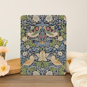 May include: A rectangular decorative panel featuring a detailed floral and bird pattern. The design includes birds, flowers, and berries in shades of blue, green, beige, and red against a dark blue background. The panel is placed on a wooden surface.