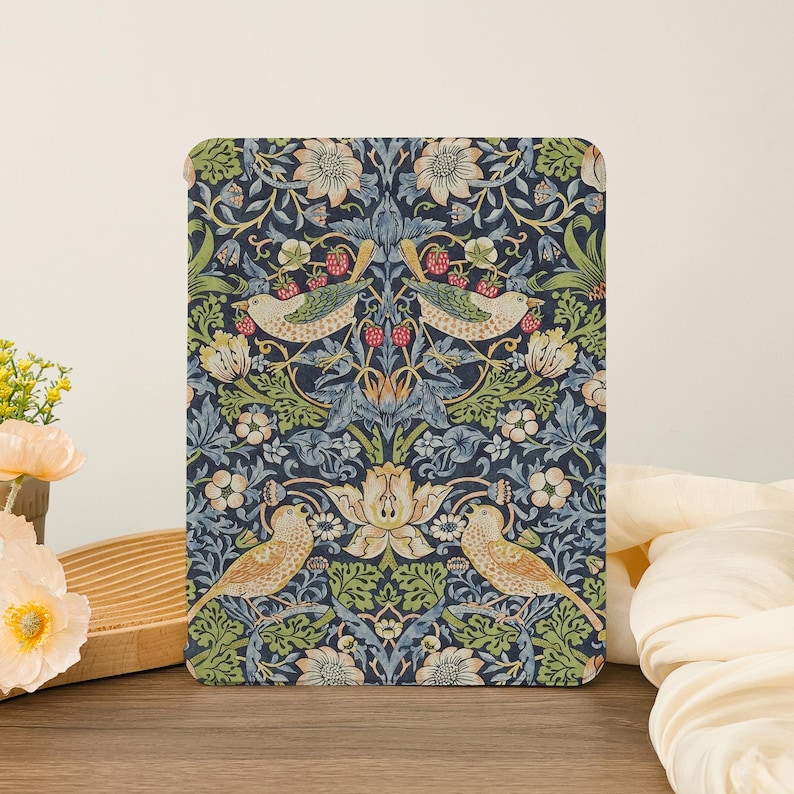 May include: A rectangular decorative panel featuring a detailed floral and bird pattern. The design includes birds, flowers, and berries in shades of blue, green, beige, and red against a dark blue background. The panel is placed on a wooden surface.