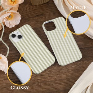 May include: Two phone cases with a vertical striped pattern in light green and white. One case is labeled "Glossy" and the other is labeled "Matte". The cases are displayed on a wooden surface with floral accents.