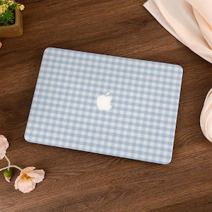 Könnte beinhalten: Eine hellblau-weiß karierte Laptop-Hülle mit dem Apple-Logo in der Mitte. Die Hülle ist rechteckig und passt auf die Oberseite eines Laptops. Der Hintergrund ist eine dunkelbraune Holzoberfläche.