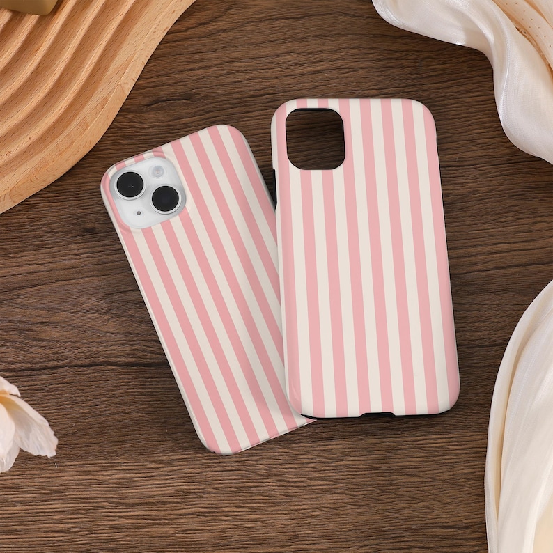May include: Two phone cases for an iPhone, featuring a pink and white striped design. The cases are made from a hard plastic material and have a smooth finish.