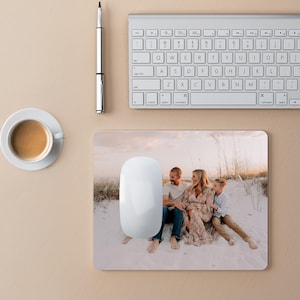 Peut inclure: Un tapis de souris blanc avec une photo d'une famille de trois personnes sur une plage. La famille est assise sur le sable, et le soleil se couche &agrave; l'horizon. Le tapis de souris est un excellent moyen de personnaliser votre espace de travail.