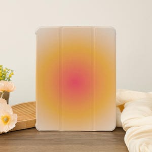 Puede incluir: Una funda transparente para tableta con un diseño degradado. La funda tiene un degradado amarillo, naranja y rosa que se desvanece del centro hacia los bordes.