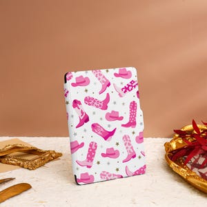 May include: A white e-reader case with a pink and white pattern of cowboy boots and hats. The case has a white background with pink stars.
