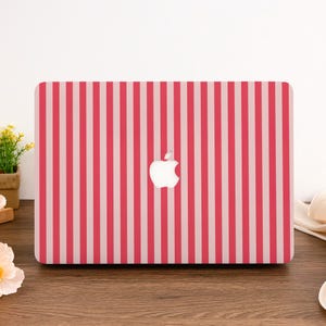 Może przedstawiać: Etui na laptopa z pionowym wzorem w paski w odcieniach różu i bieli. Logo Apple jest widoczne na środku. Etui znajduje się na drewnianej powierzchni.