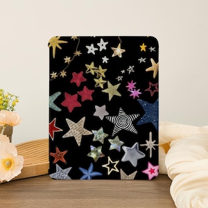 Op de afbeelding: Een zwarte achtergrond met een verscheidenheid aan kleurrijke sterren, waaronder rood, goud, blauw en roze. De sterren zijn van verschillende groottes en vormen, en sommige hebben een glinsterende afwerking.