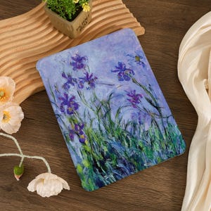 May include: A tablet case featuring a floral painting of purple irises and green grass against a blue background. The artwork is reminiscent of impressionist art. The case is rectangular and has rounded corners.