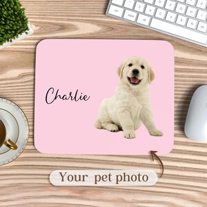 May include: Pink mouse pad with a white dog on it. The dog is sitting and looking at the camera. The text "Charlie" is written on the mouse pad.