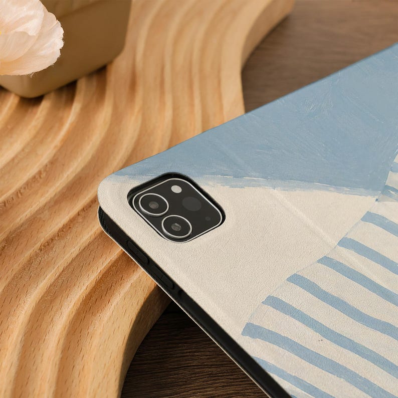 Puede incluir: Una funda para tableta con un dise&ntilde;o pintado. La funda presenta una combinaci&oacute;n de colores azul claro y blanco con un patr&oacute;n de rayas y una secci&oacute;n azul s&oacute;lida. La lente de la c&aacute;mara es visible en la funda.